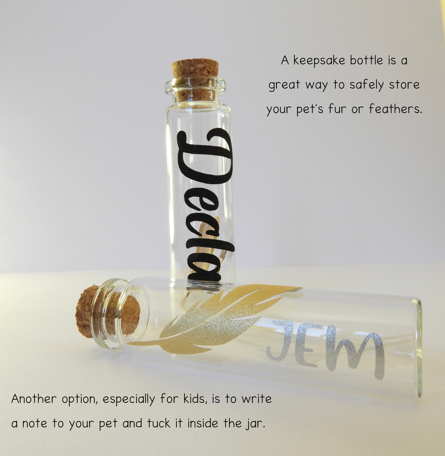 The photo displays two glass keepsake bottles with charms and vinyl lettering for the pet’s name. A keepsake bottle is a great way to store your pet’s fur, whiskers, or feathers.