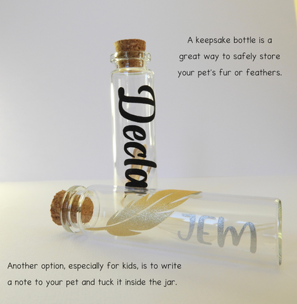 The photo displays two glass keepsake bottles with charms and vinyl lettering for the pet’s name. A keepsake bottle is a great way to store your pet’s fur, whiskers, or feathers.