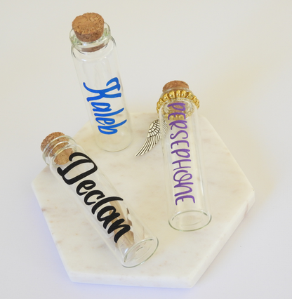 The photo displays three glass keepsake bottles with vinyl lettering for the pet’s name. 